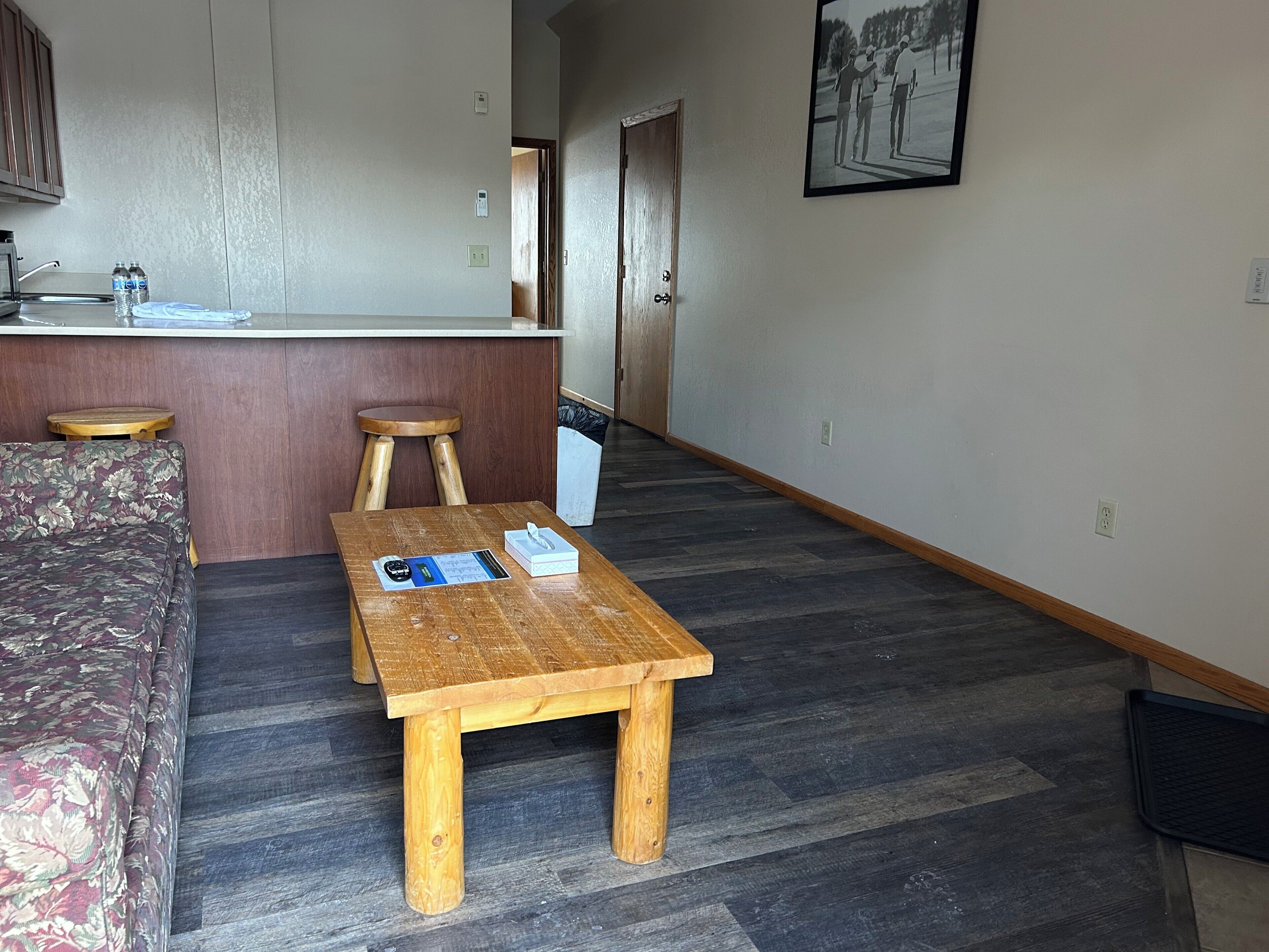 A room with a wooden bench, a floral sofa, a small table with a menu, and a kitchen area with a counter and stools.