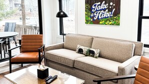 Una sala de estar moderna con un sofá, sillones, una mesa de centro y un cuadro en la pared.