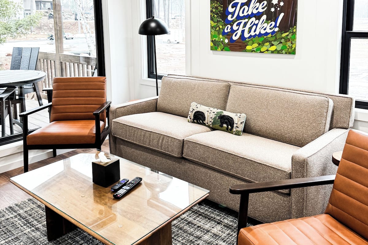 A modern living room with a sofa, armchairs, a coffee table, and a painting on the wall.