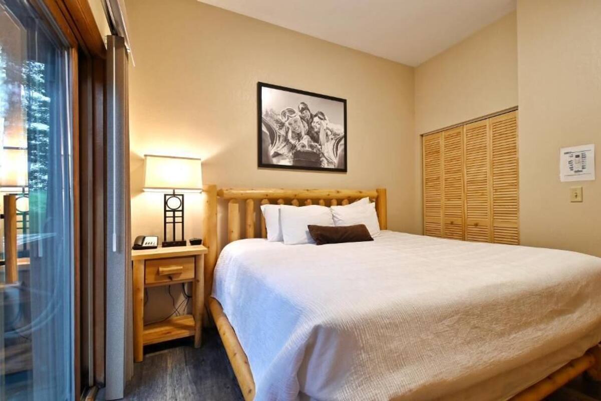 A hotel room with a bed, a nightstand, a lamp, a framed picture on the wall, and a window with curtains.