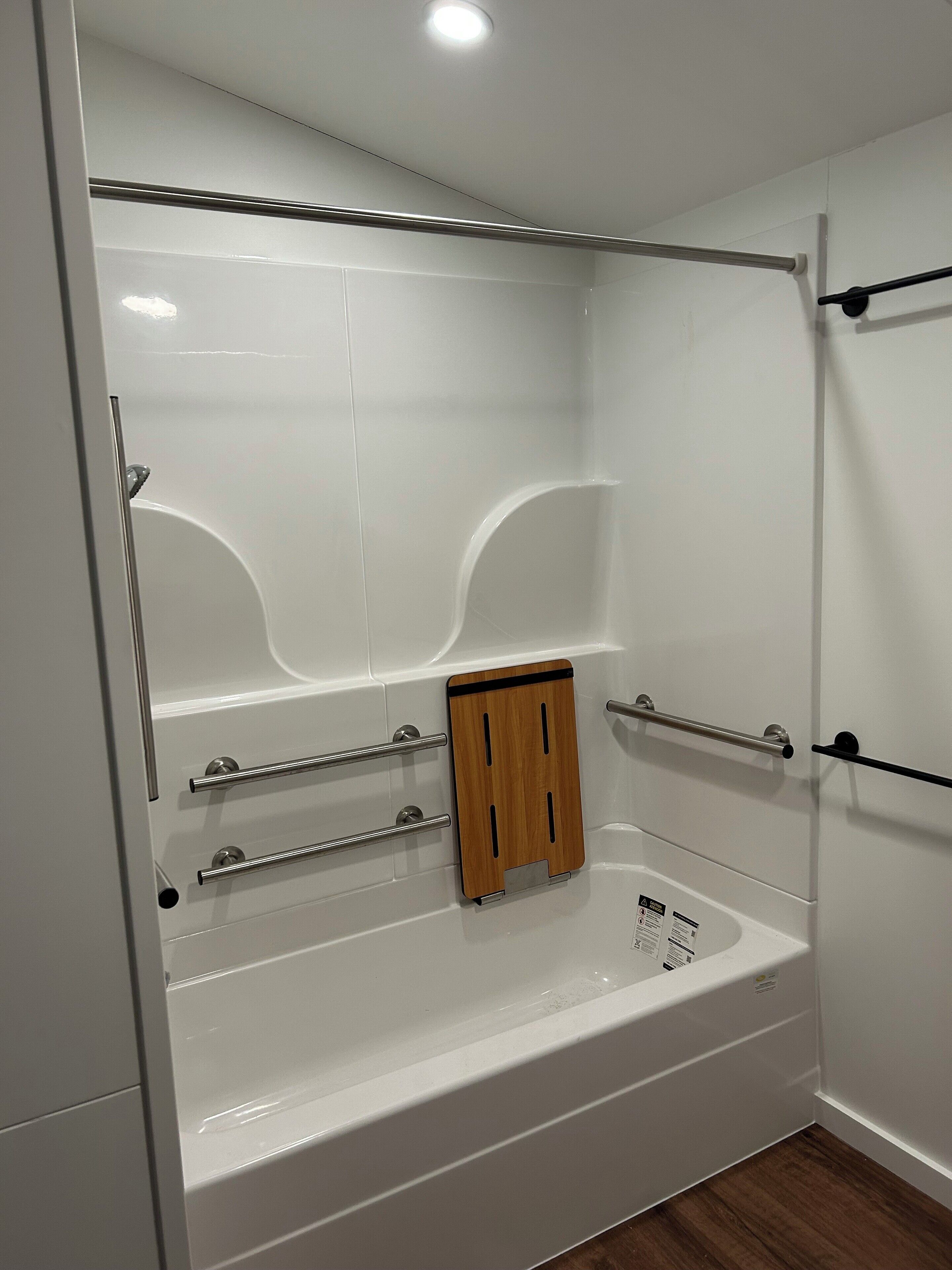 A modern bathroom with a white bathtub, wooden bath tray, and metal handrails.