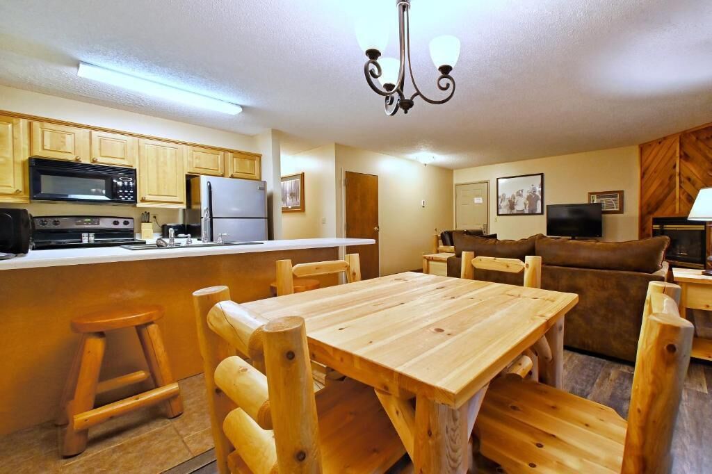 A compact kitchen with wooden cabinets, a microwave, stove, refrigerator, and a dining area with a wooden table and chairs.