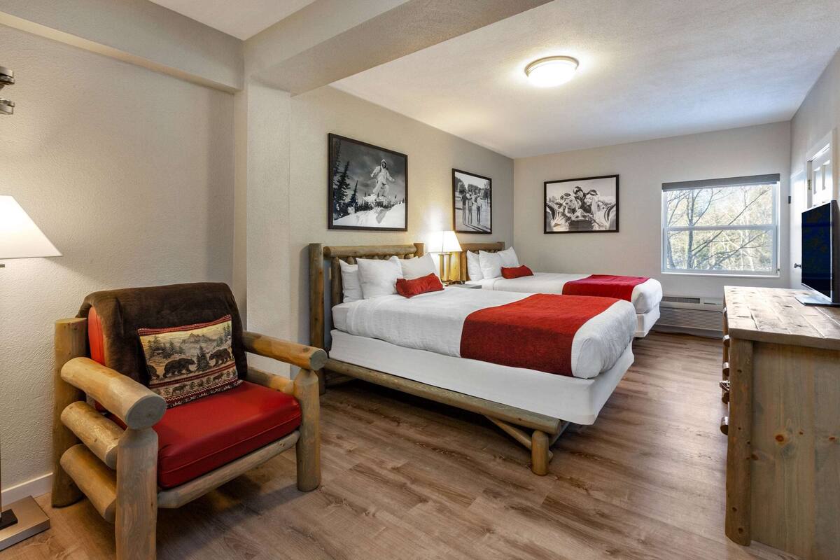 A hotel room with a wooden bed, a chair with a red cushion, and a television on a wooden stand.