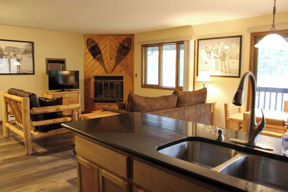 A cozy living room with a fireplace, a sofa, a TV, and a large window.