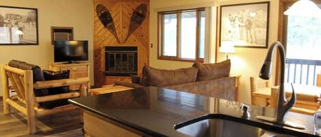 A cozy living room with a fireplace, a sofa, a TV, and a large window.