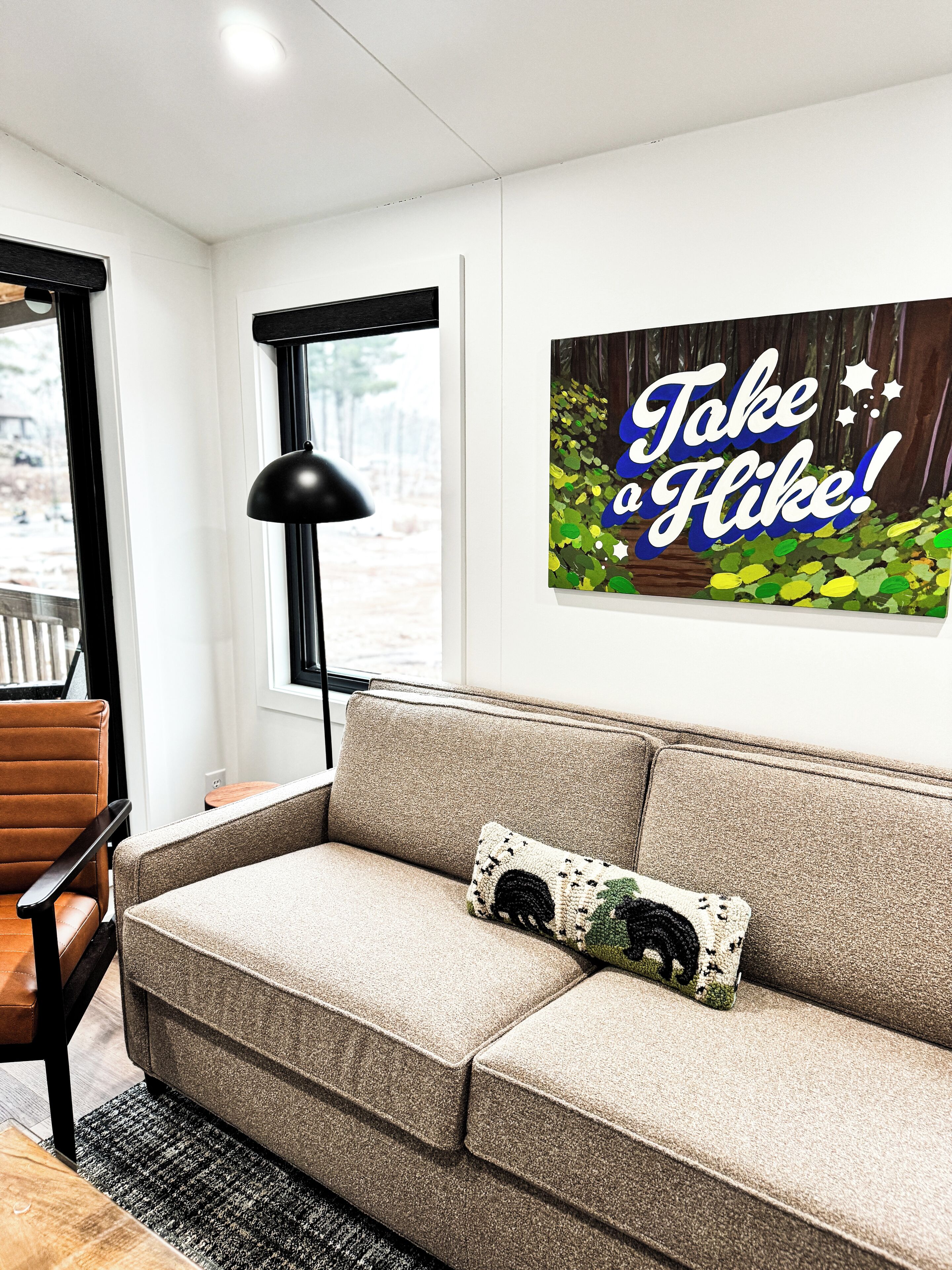 Ein modernes Wohnzimmer mit einem beigen Sofa, einer schwarzen Lampe und einem motivierenden Poster an der Wand.
