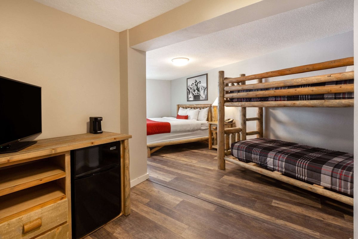 A compact hotel room with a wooden desk, a television, a bunk bed, and a small kitchenette.