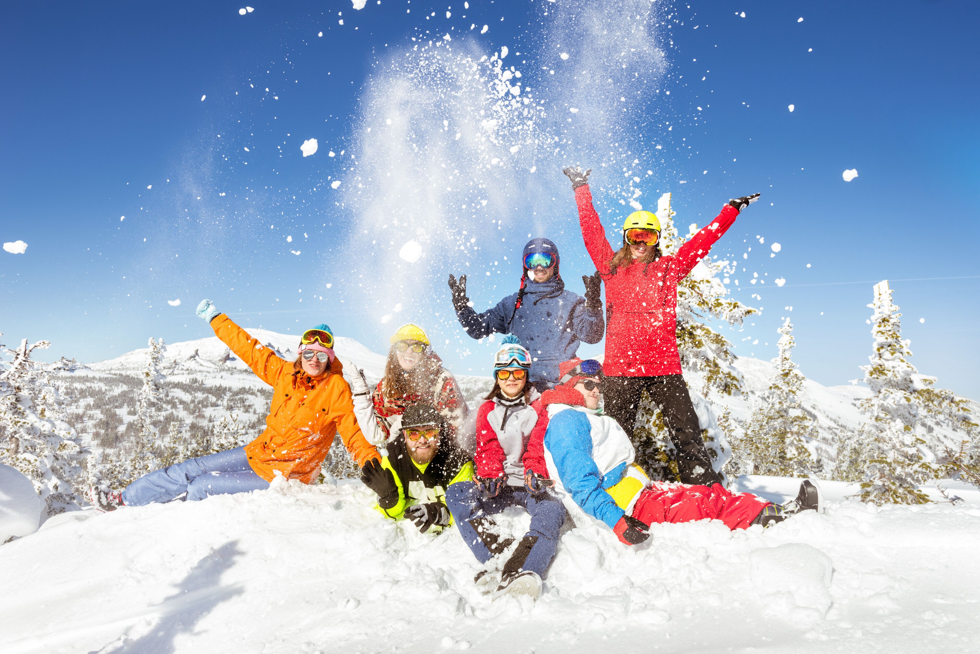 A group of people in a snowy outdoor setting with trees and a clear sky.