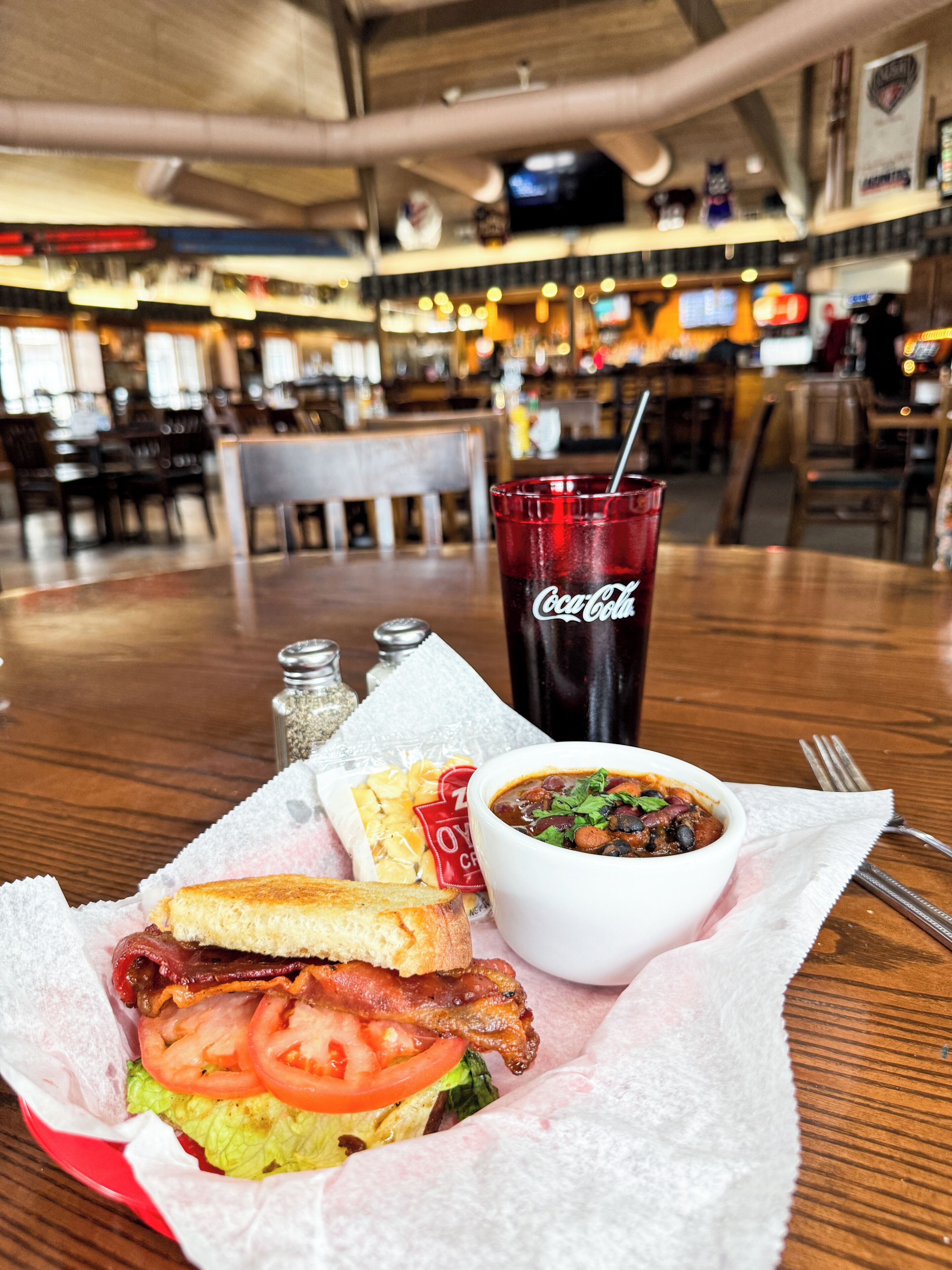 A meal consisting of a sandwich, soup, and a Coca-Cola drink on a table in a restaurant.