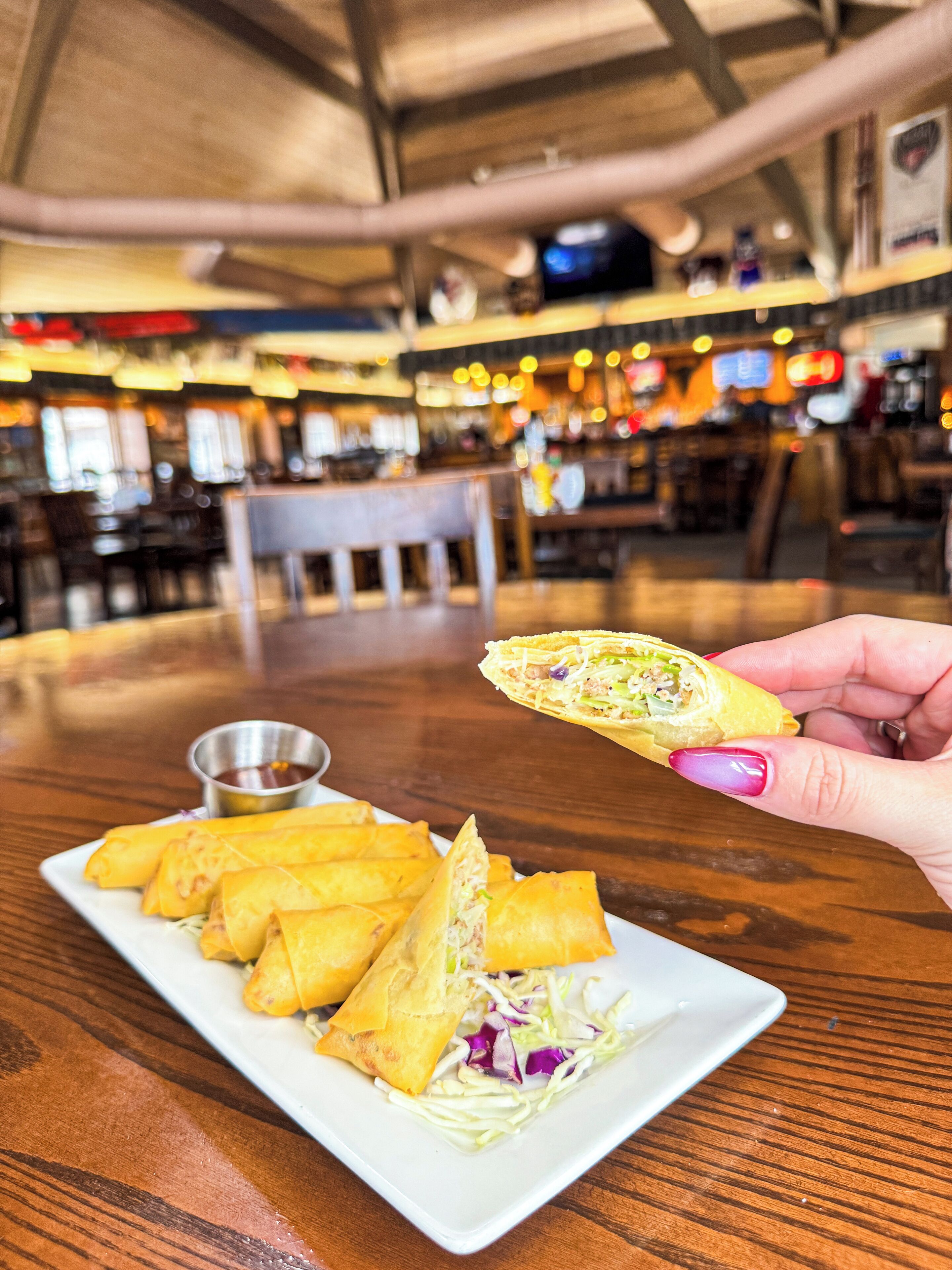 A hand holding a spring roll over a plate with several spring rolls and a side salad.