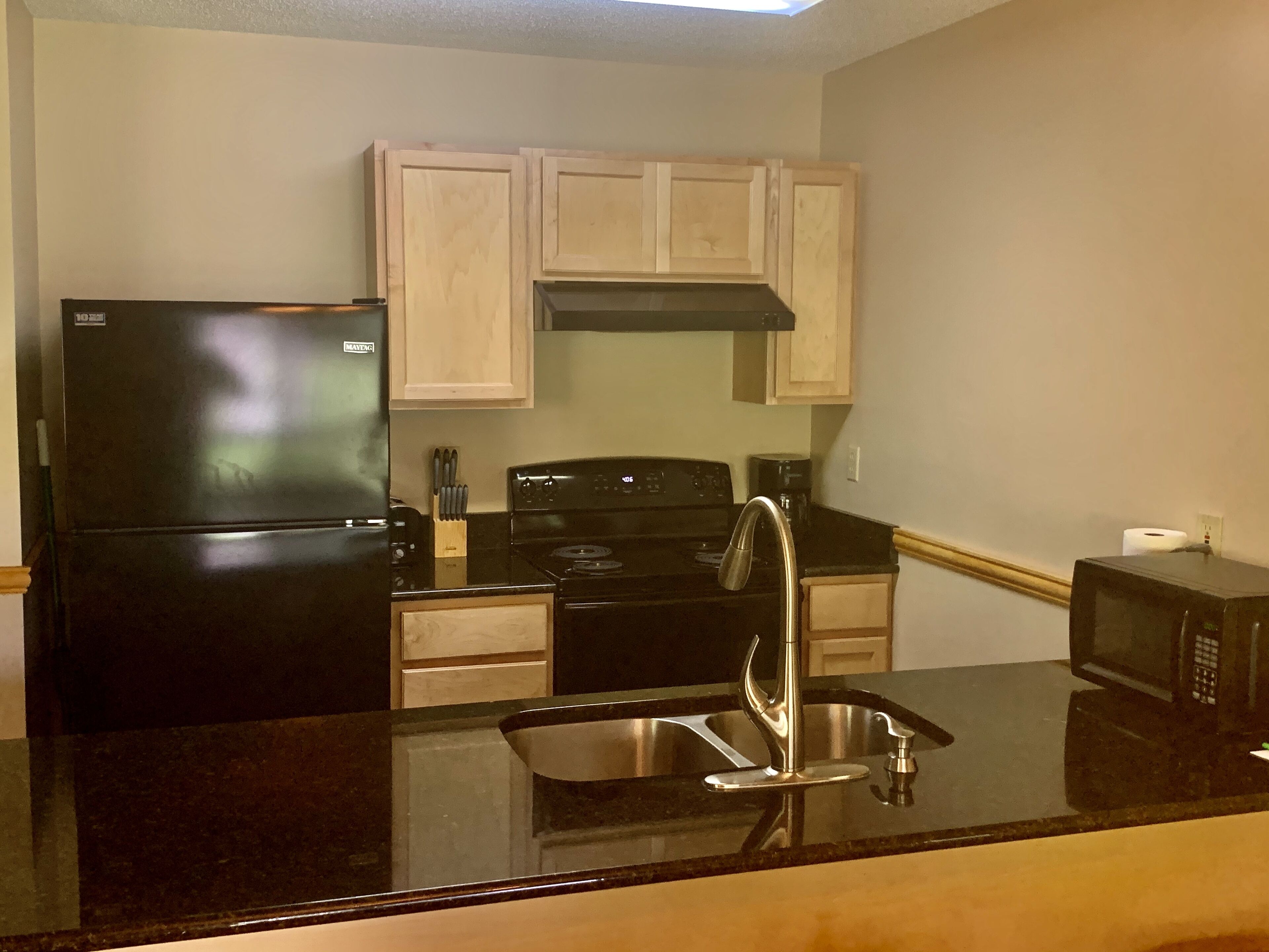 A kitchen with a black refrigerator, stove, and microwave, wooden cabinets, and a stainless steel sink.