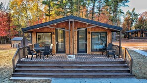Een houten hut met terras, zitplaatsen buiten en grote glazen deuren.