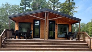 Una cabaña de madera con terraza techada, puertas correderas grandes de vidrio y un conjunto de mobiliario exterior.