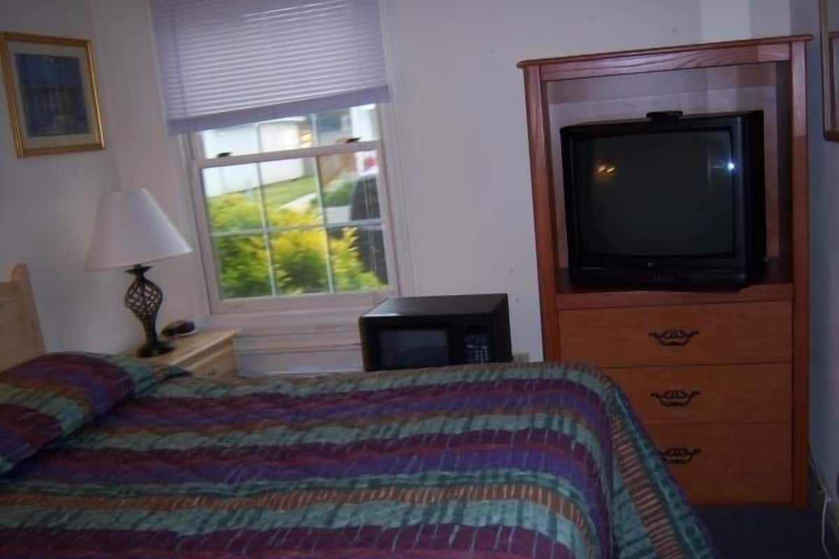 A bedroom with a bed, a television, a lamp, and a window.