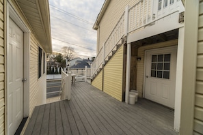 A narrow wooden deck with a white door and a garage door on the right.