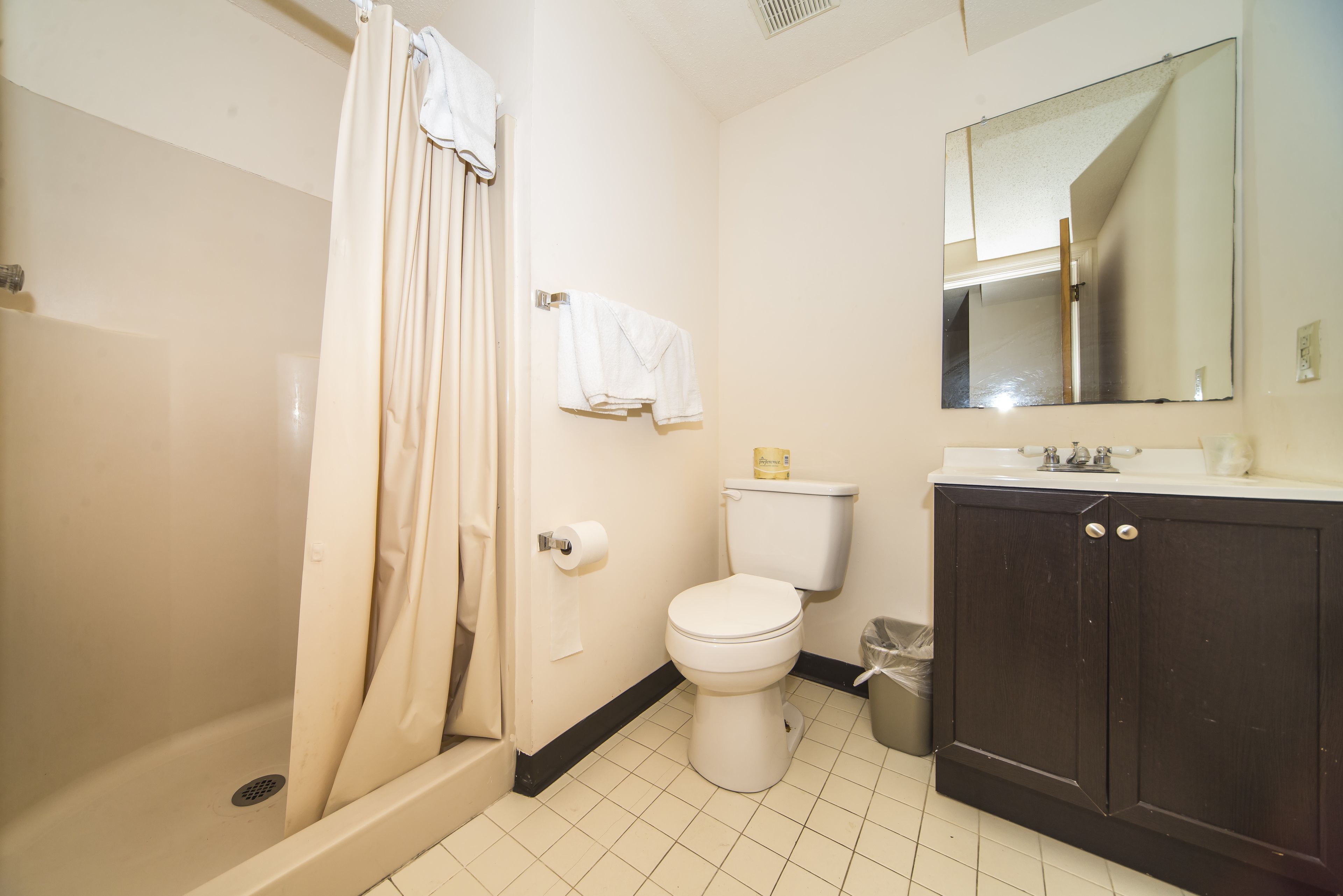 A bathroom with a shower, toilet, sink, and mirror.