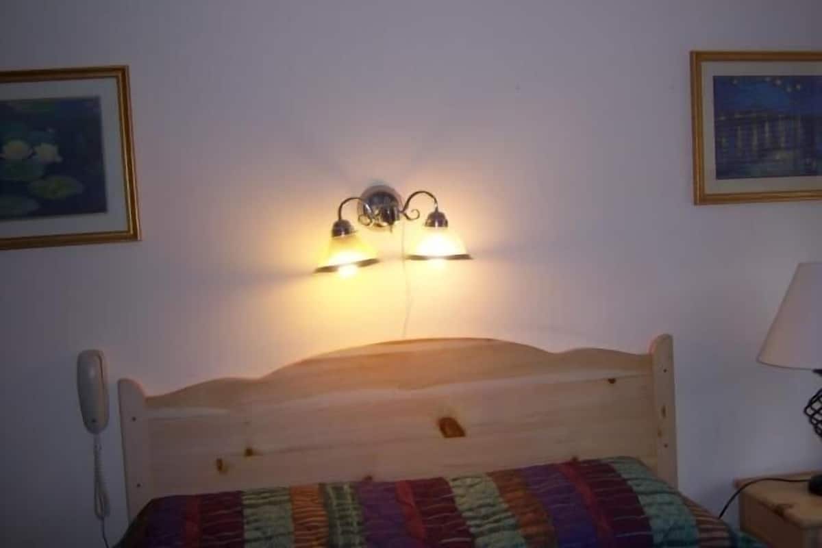 A room with a wooden bed, a telephone on the wall, and two wall-mounted light fixtures.