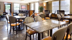 A spacious dining area with multiple tables and chairs, large windows, and a potted plant. - Drury Inn & Suites San Antonio North Stone Oak (San Antonio)