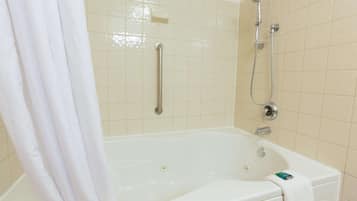 Una bañera blanca con cabezal de ducha y barra de apoyo, una toalla colgada en el lateral y un jabonera en la pared.