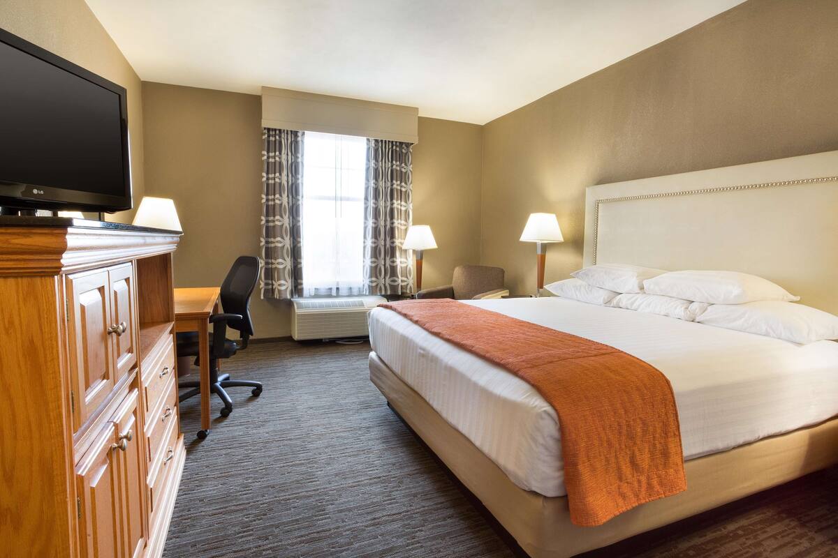 Une chambre d’hôtel avec un lit, un bureau, une télévision et une fenêtre avec des rideaux.