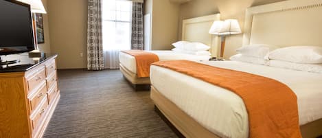 A hotel room with two beds, a TV, a dresser, and a window with curtains.