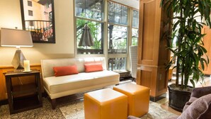 A cozy living area with a sofa, ottomans, a lamp, and a potted plant. - Drury Inn & Suites San Antonio North Stone Oak (San Antonio)