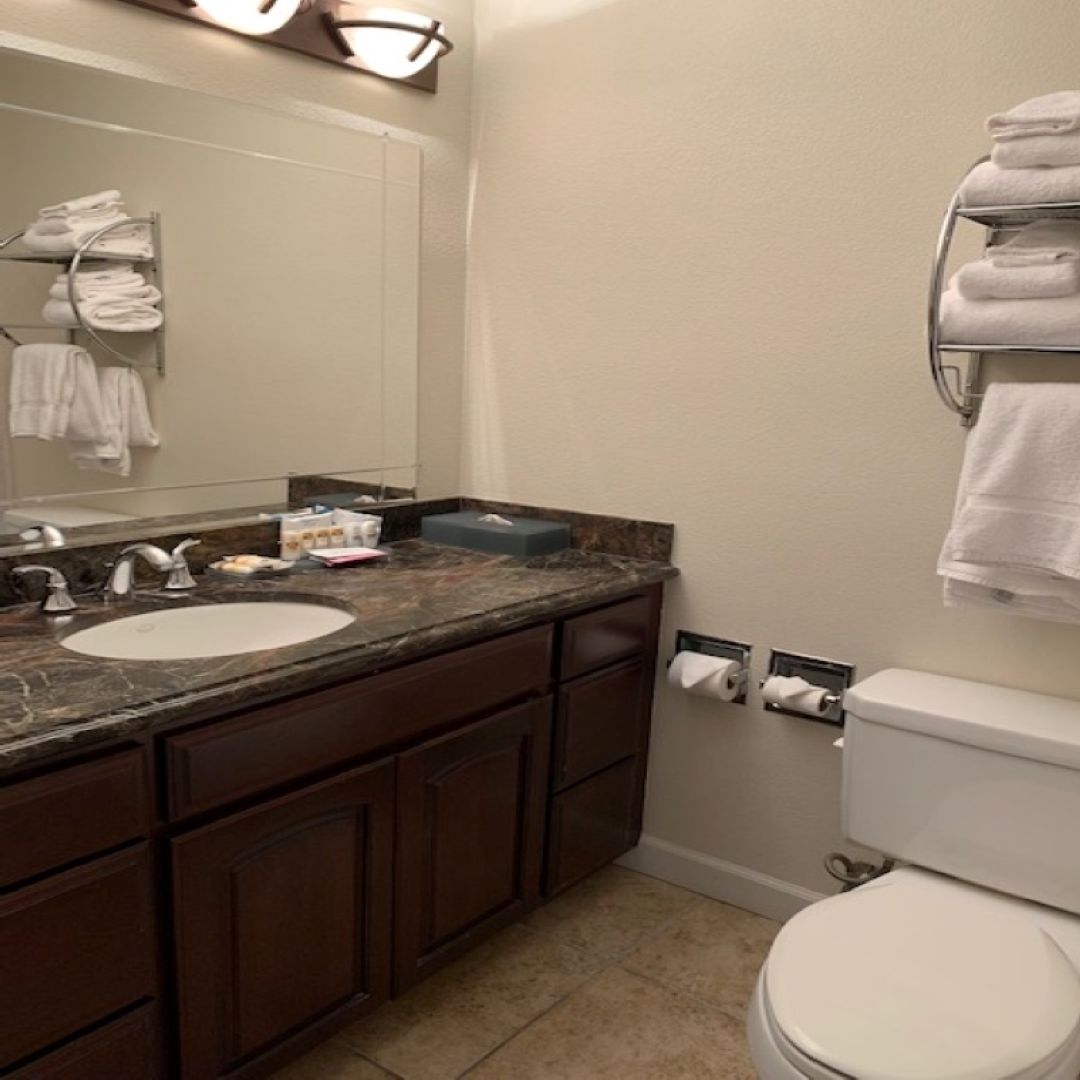 A bathroom with a marble sink, dark wooden cabinets, a white toilet, and a towel rack with folded towels.