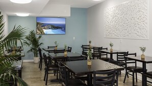 Una sala de conferencias con una gran pantalla plana en la pared, varias mesas y sillas, y paneles decorativos.