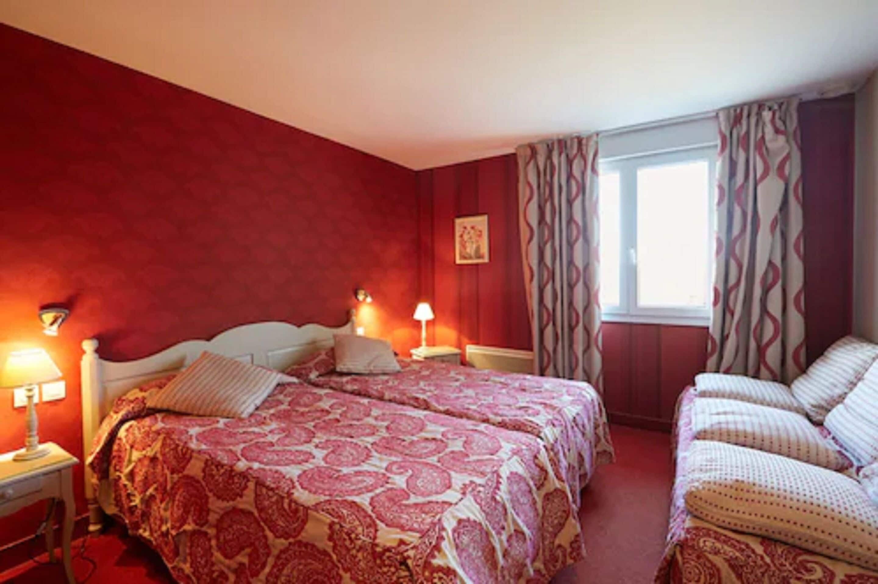 Una habitación con dos camas, paredes rojas y una ventana con cortinas.