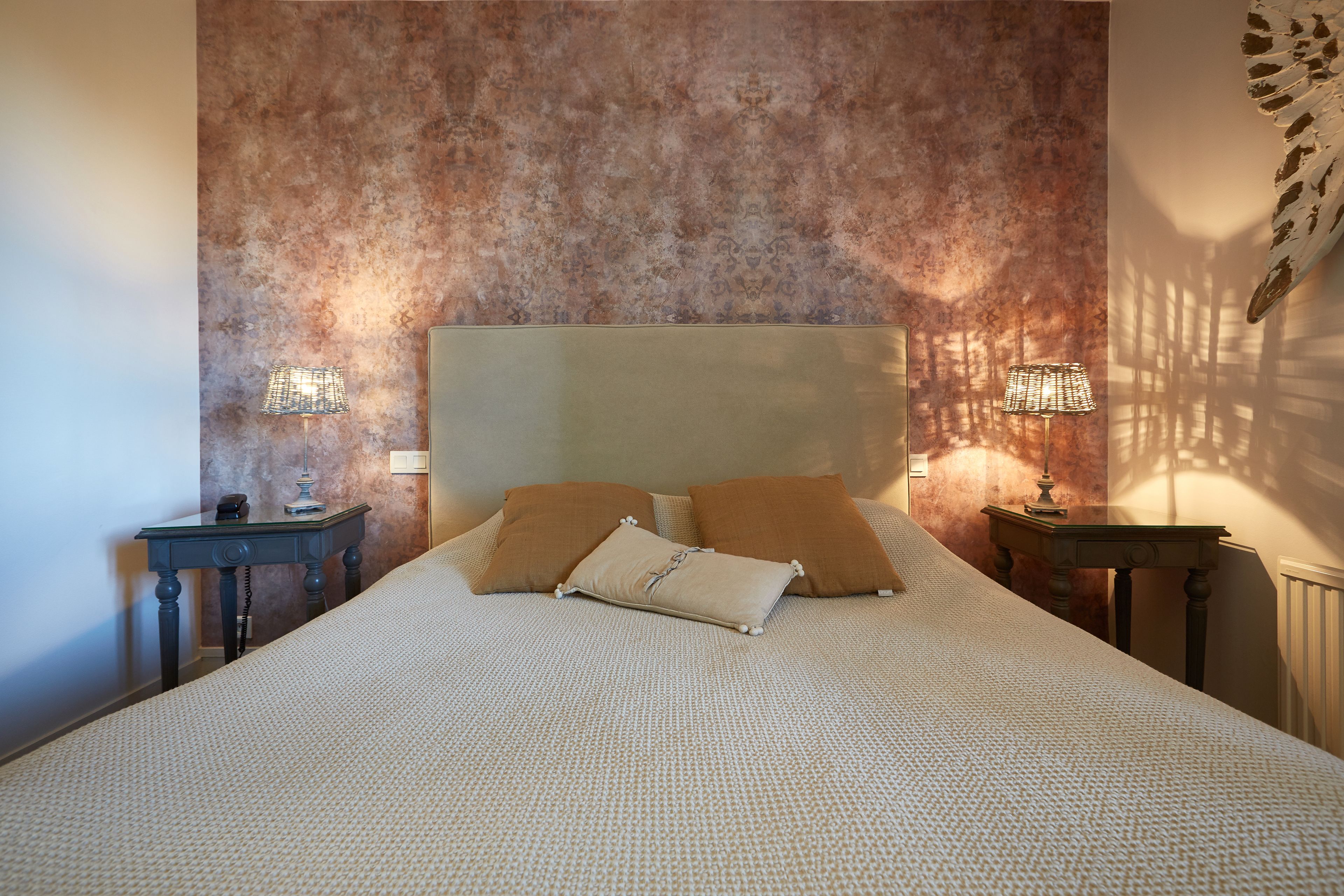 A neatly made bed with a textured headboard, two bedside tables with lamps, and a wall with a textured pattern.