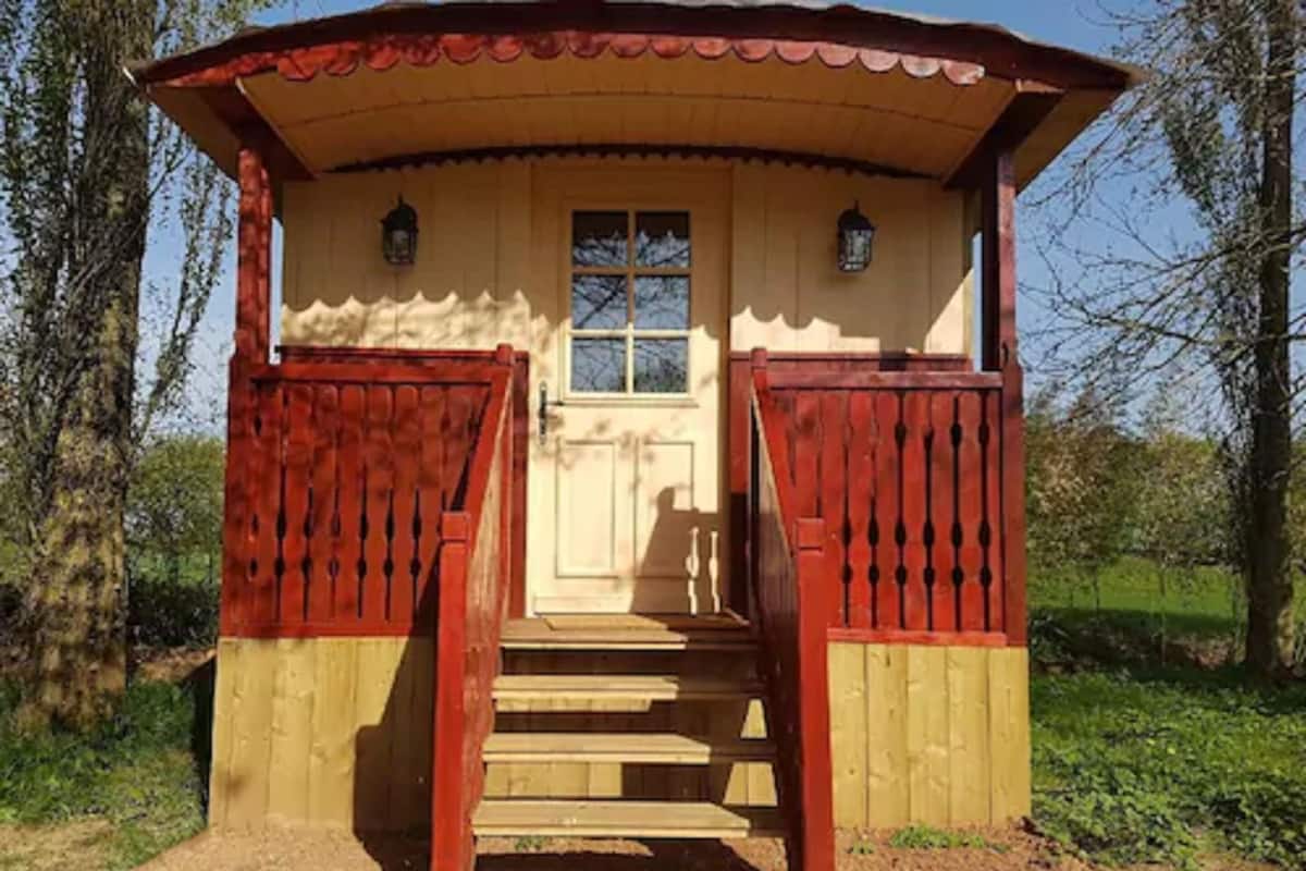 Une petite cabane en bois avec une porte et des fenêtres rouges, un escalier menant à une porte, et une rambarde rouge de chaque côté.