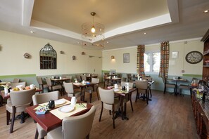 Uma sala de jantar com várias mesas e cadeiras, um candelabro e um relógio na parede.