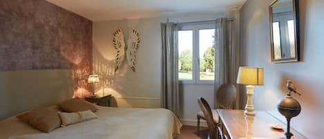 Una habitación de hotel con una cama grande, un escritorio con lámpara, una silla y una ventana con cortinas.