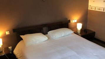 Une chambre d’hôtel avec un grand lit, deux lampes de chevet, un miroir fixé au mur et une prise électrique sur la table de chevet.