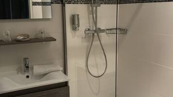 A modern bathroom with a glass-enclosed shower, a white sink with a wooden vanity, and a mirror above the sink.