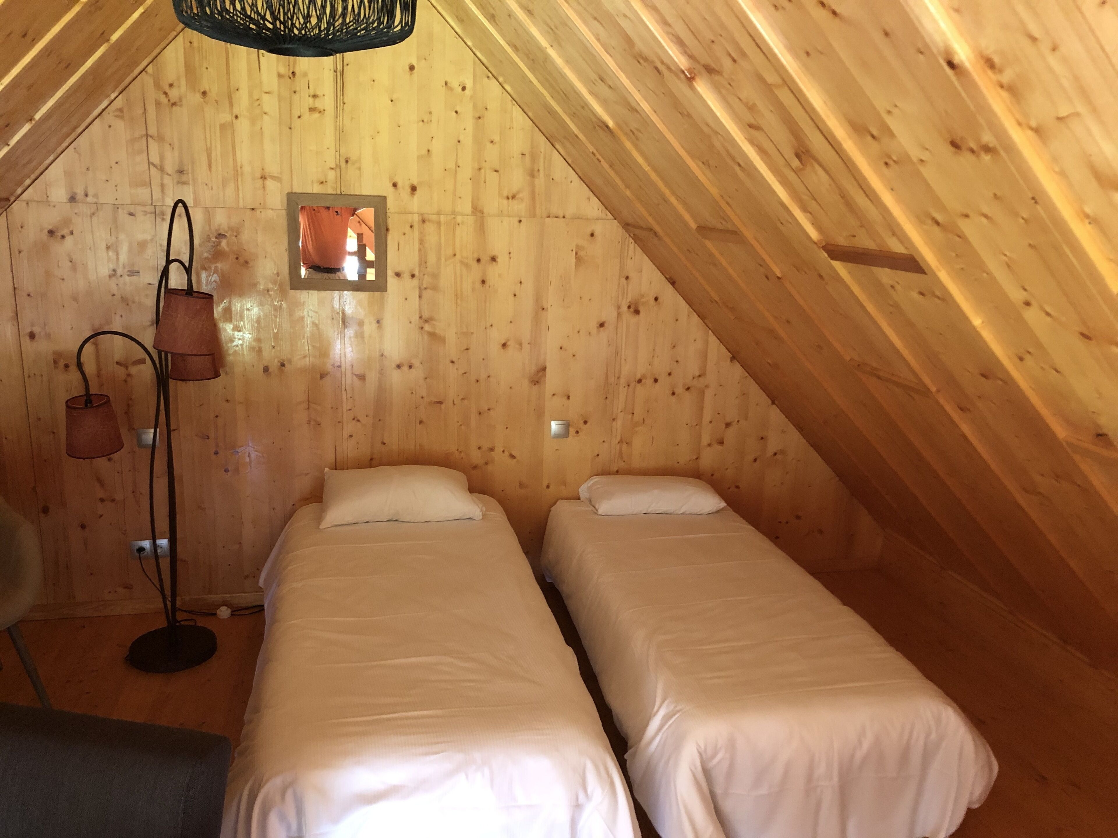 Een gezellig zolderkamer met twee eenpersoonsbedden, een klein raam en een vloerlamp.