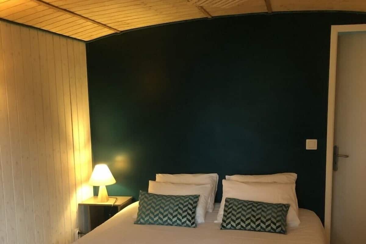 Une chambre avec un plafond en bois, un lit avec une literie blanche, deux oreillers à motifs verts et une lampe de chevet.