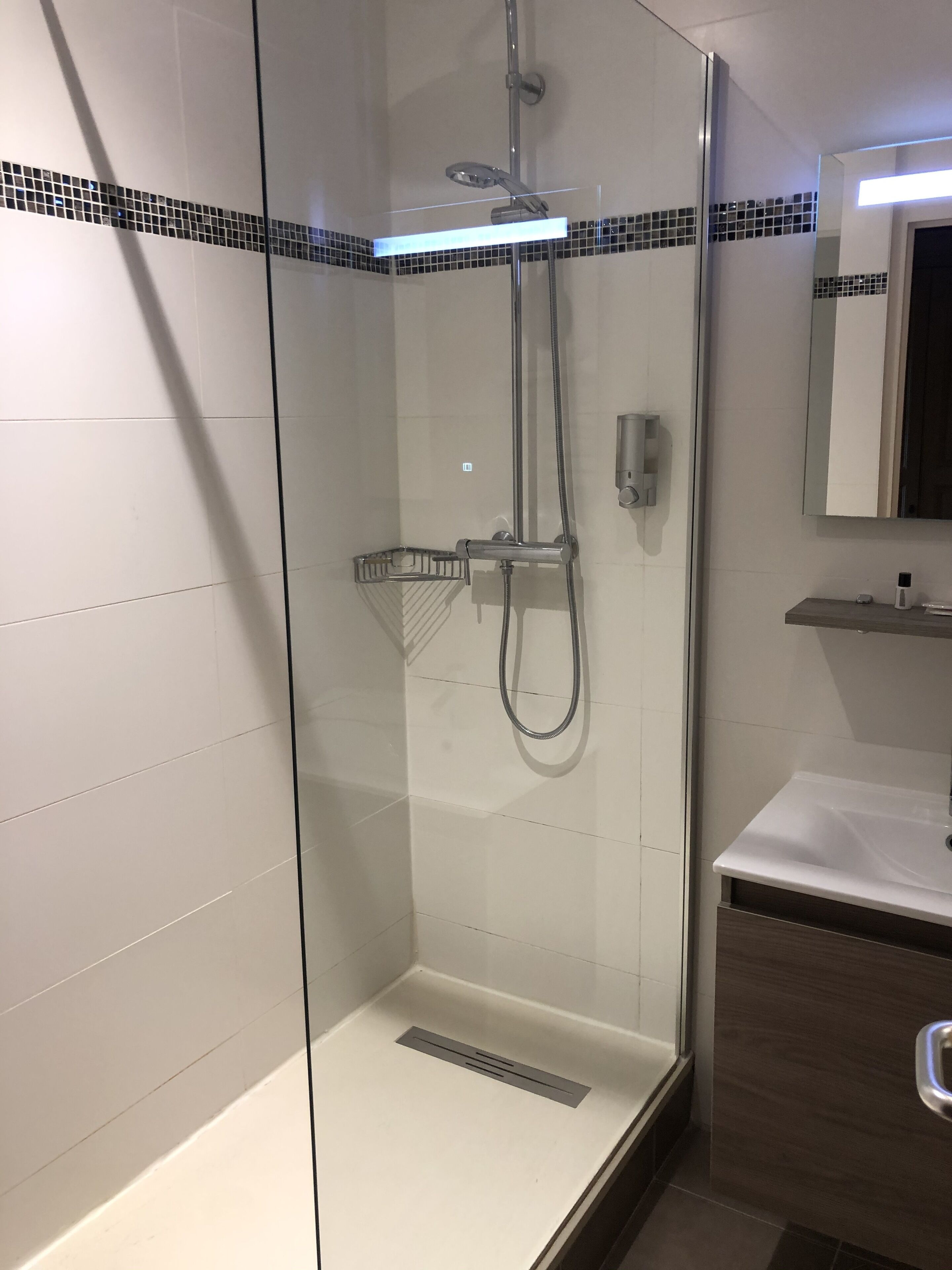 Eine begehbare Dusche mit Glaswänden, einer Handbrause und einem am Wand montierten Wasserhahn.