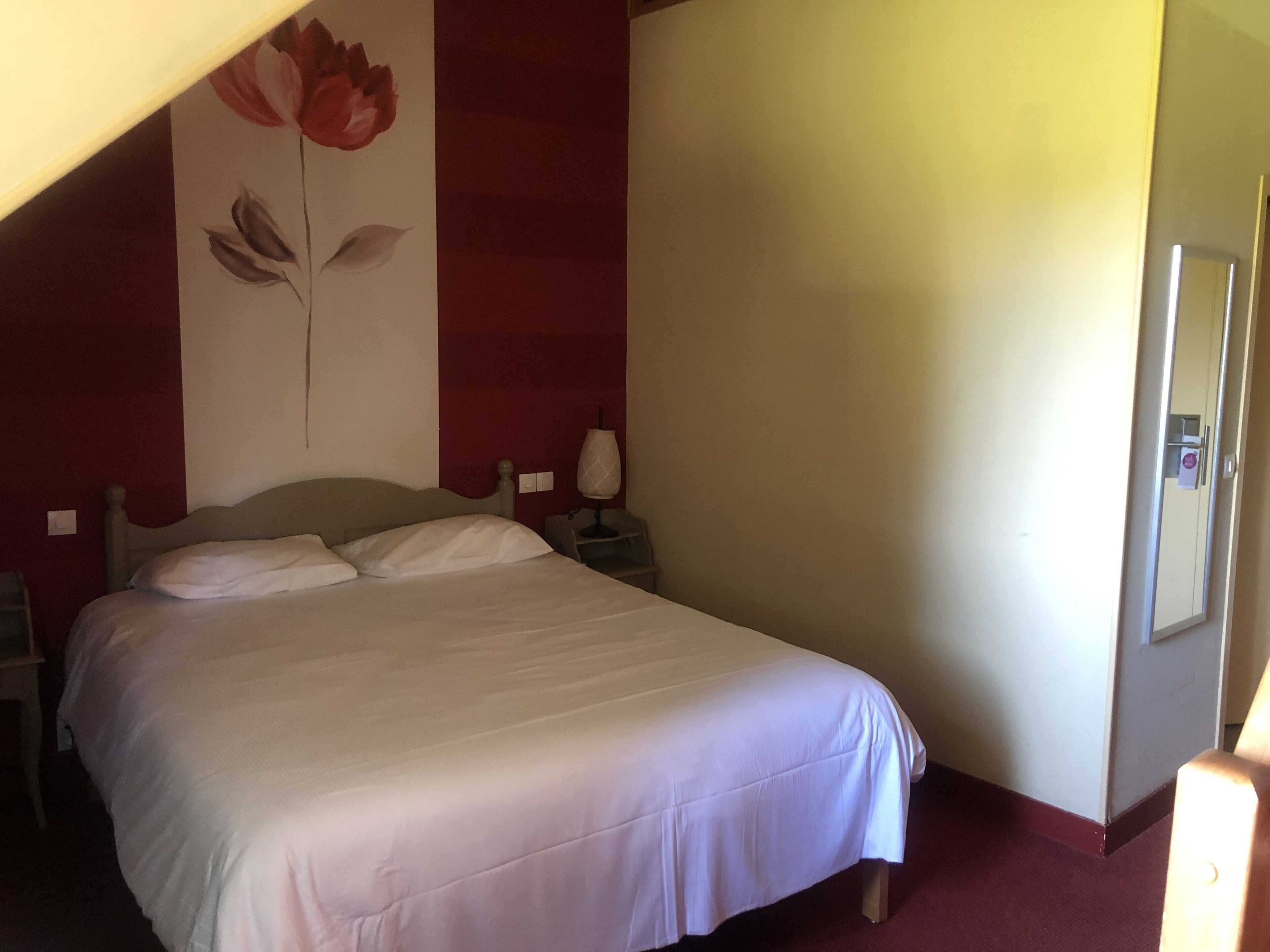 A bedroom with a bed, a nightstand, a lamp, and a wall with a floral design.
