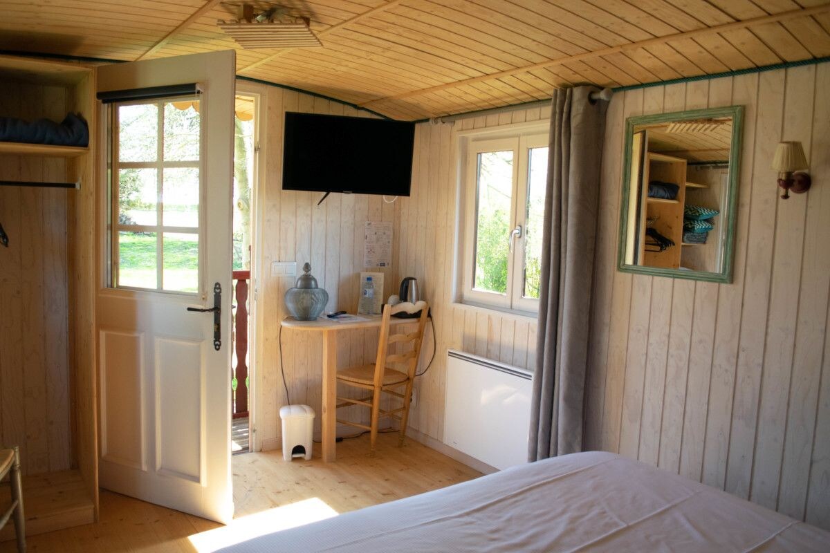 A room with a bed, a desk, a chair, a television, and a window with curtains.