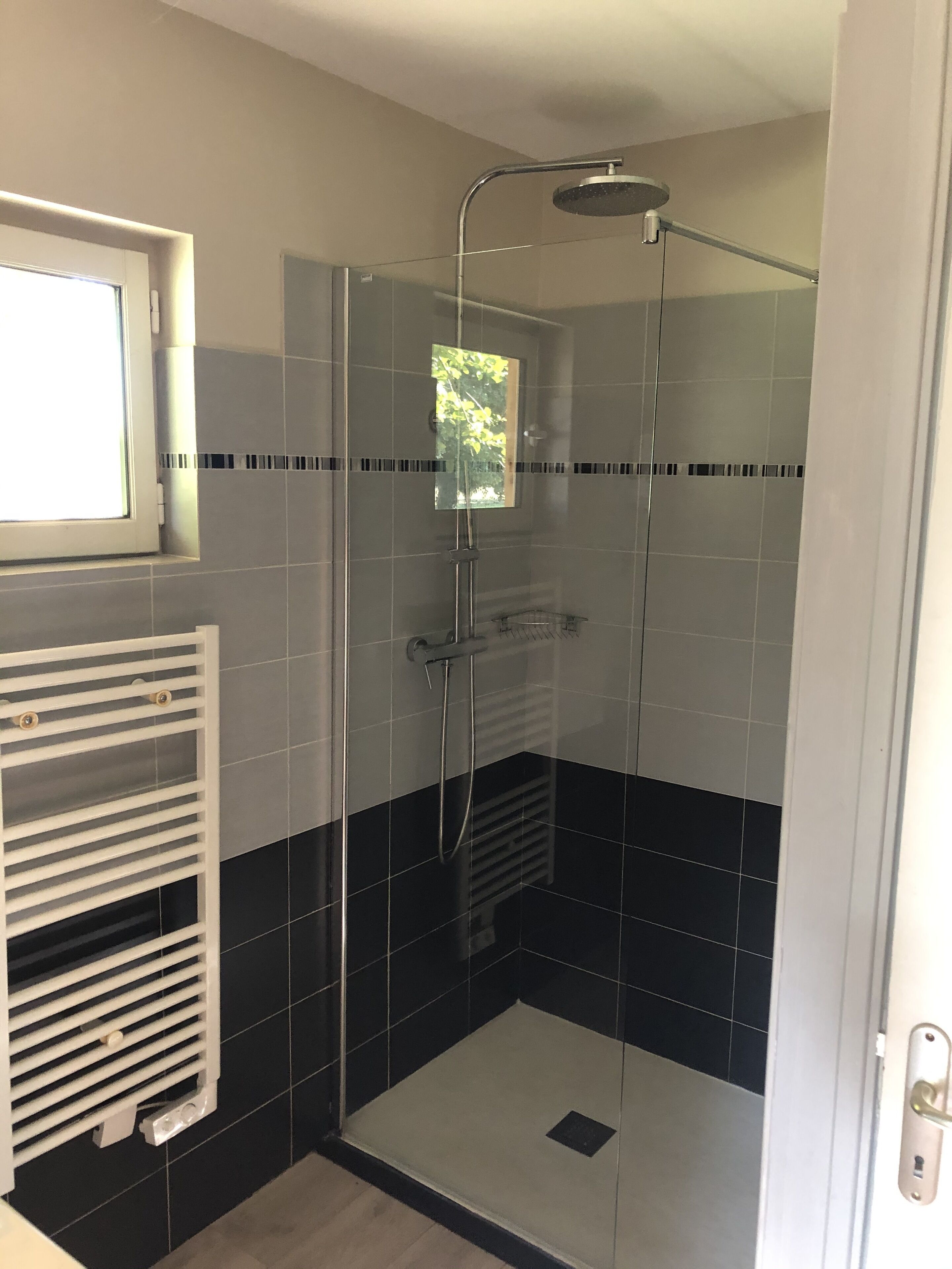 A modern bathroom with a glass-enclosed shower, a white towel rack, and a window with a view of greenery.