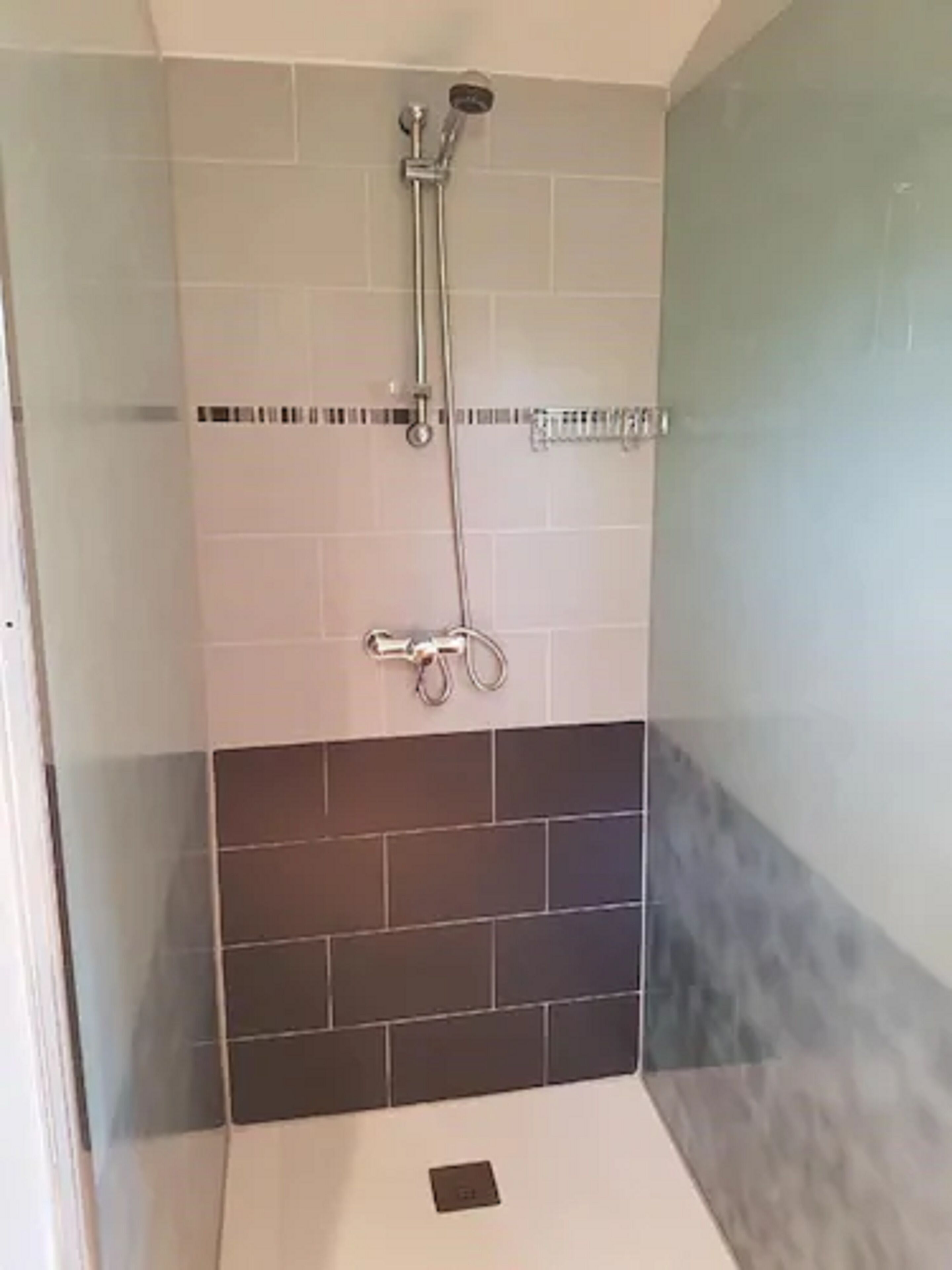 Une douche équipée d’un pommeau de douche à main et d’un robinet fixé au mur.