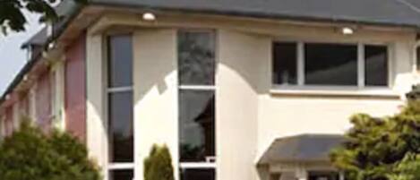 Une maison à deux étages avec un toit gris, de grandes fenêtres et une véranda à l’avant.