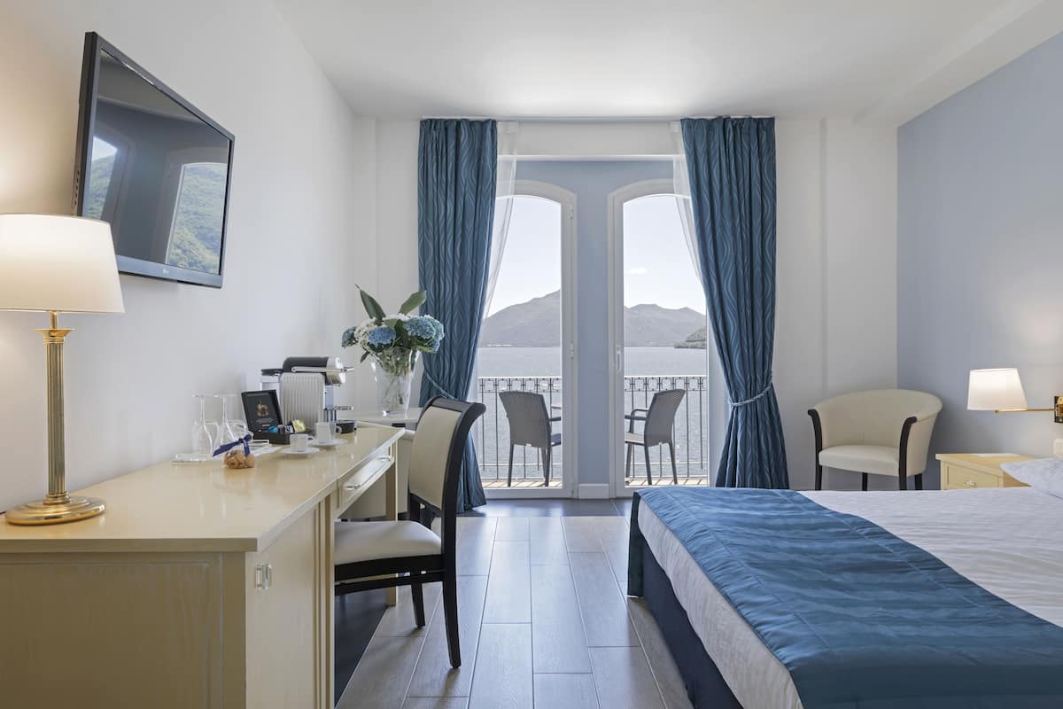 A hotel room with a bed, desk, chairs, and a balcony with a view.