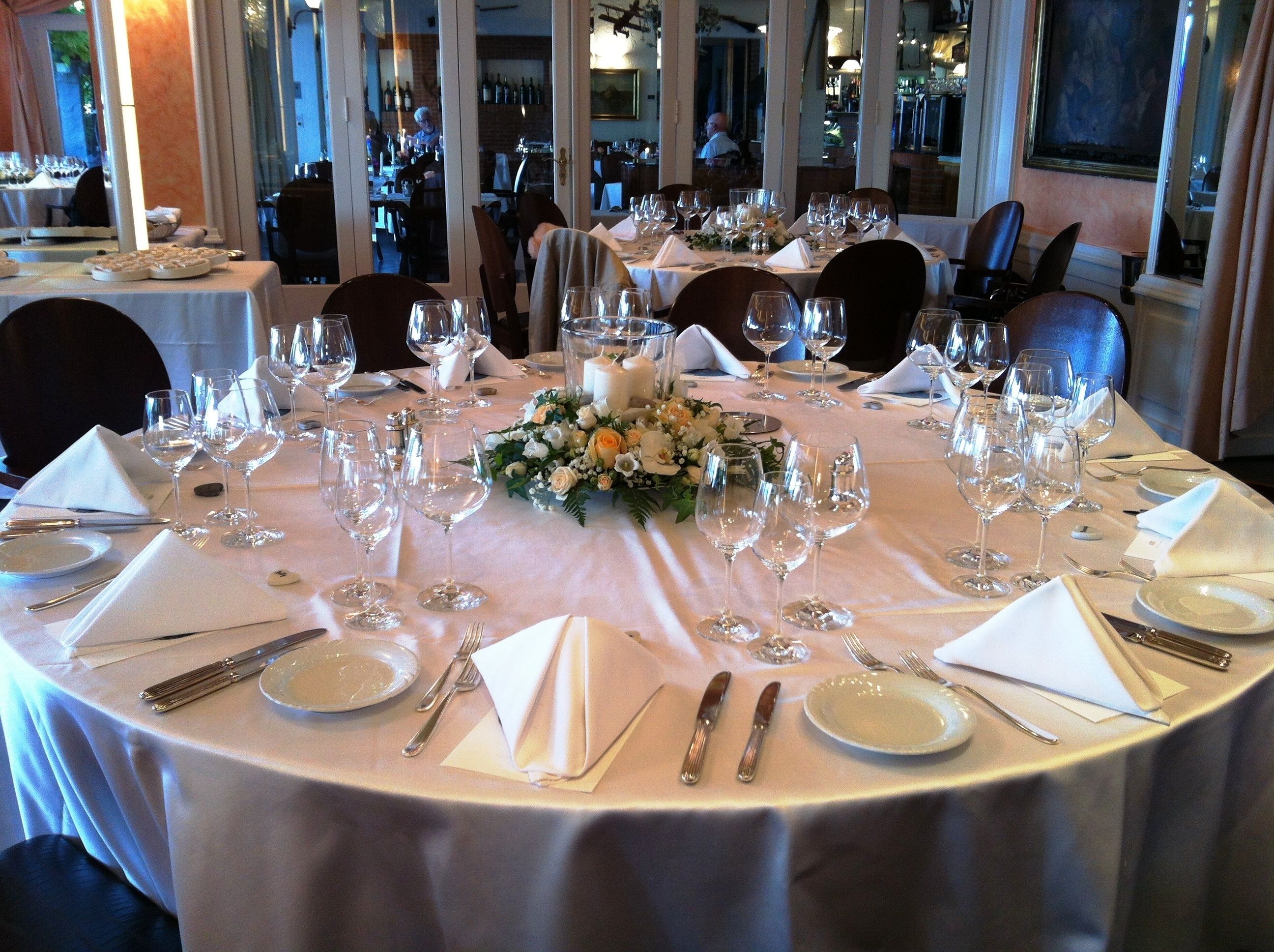 A round dining table set for a formal event with multiple wine glasses, plates, and cutlery.