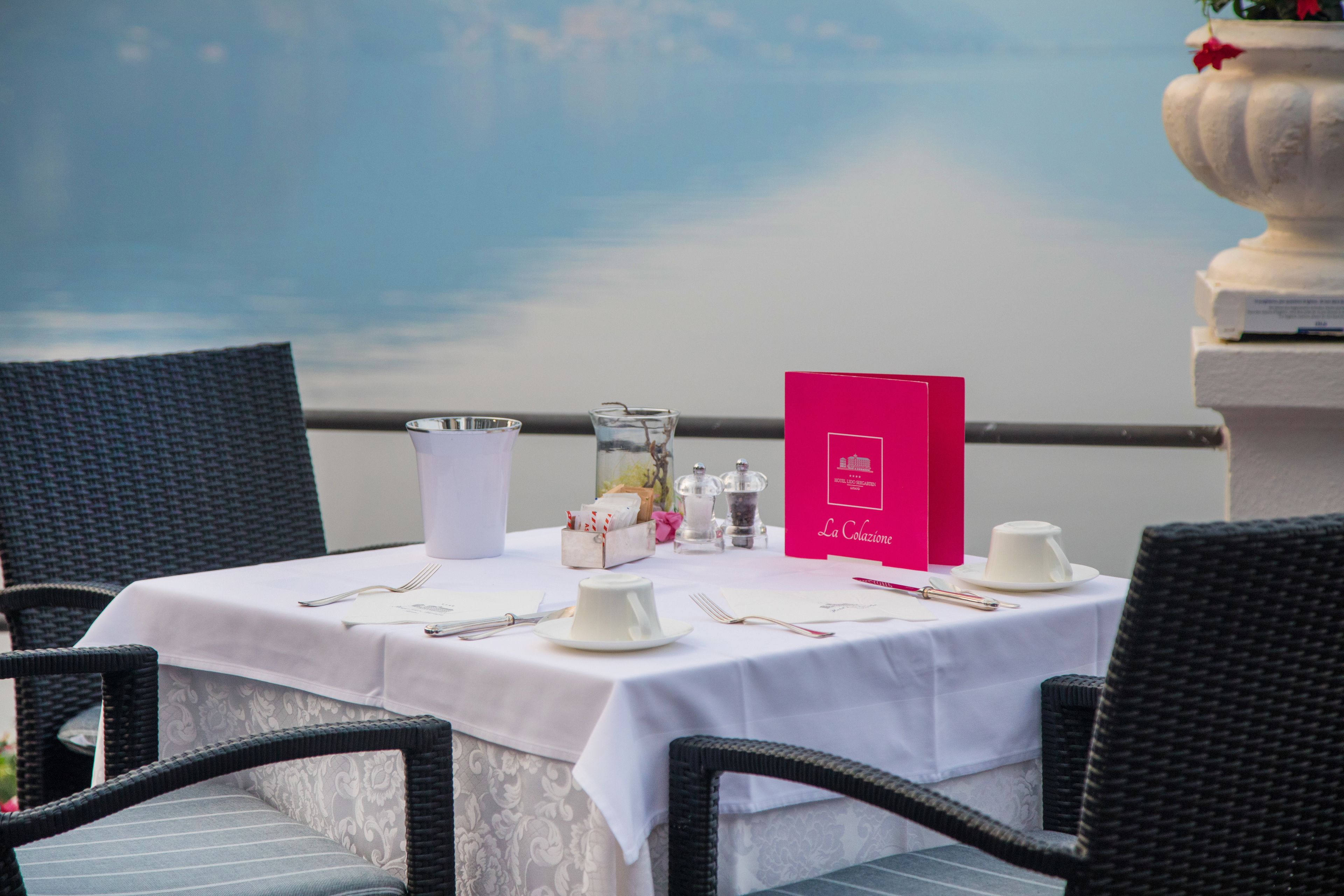 Una mesa preparada para comer, con mantel blanco, un menú y vistas al mar.
