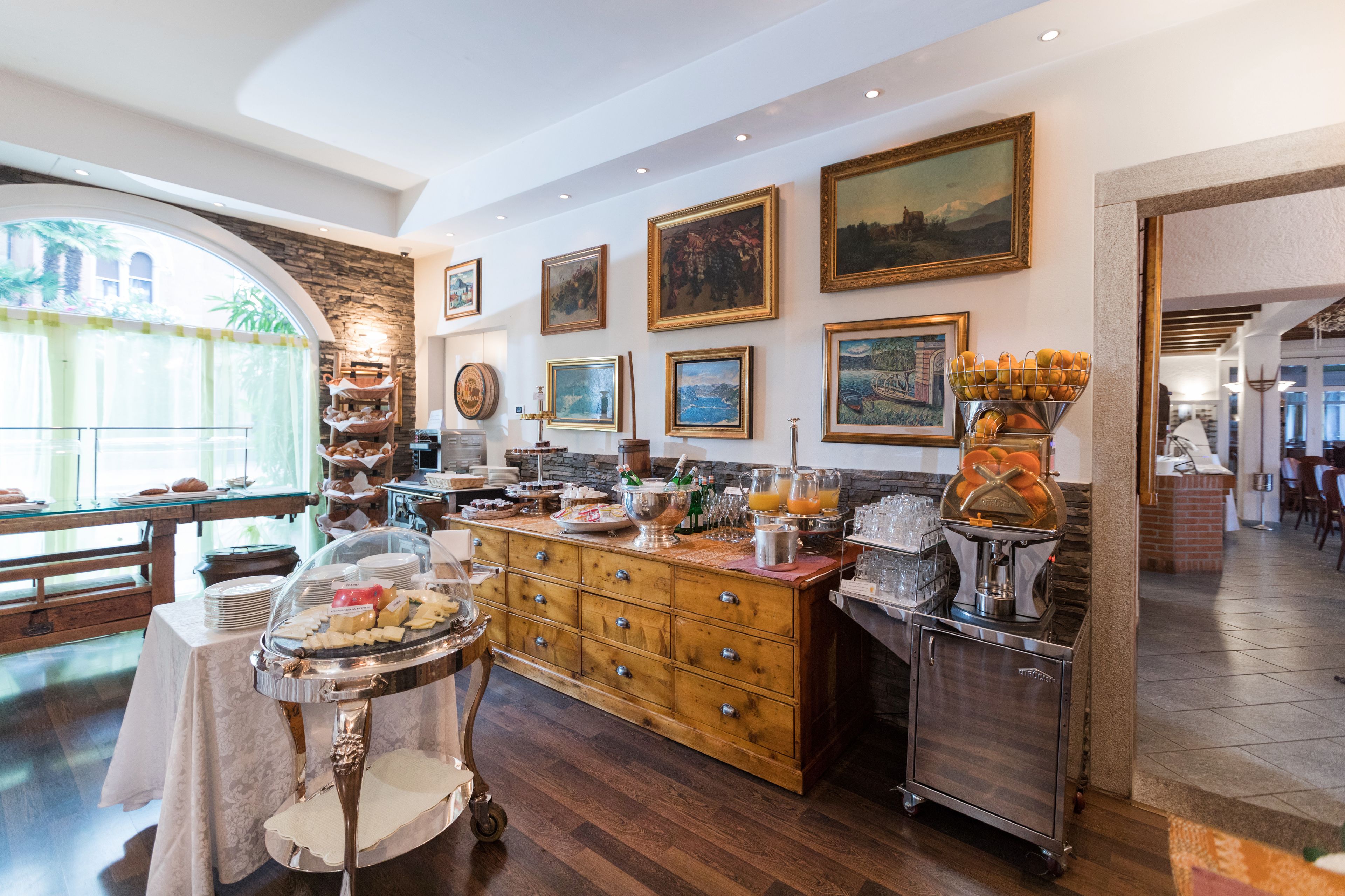 A well-lit breakfast area with a wooden buffet, a coffee station, and artwork on the walls.