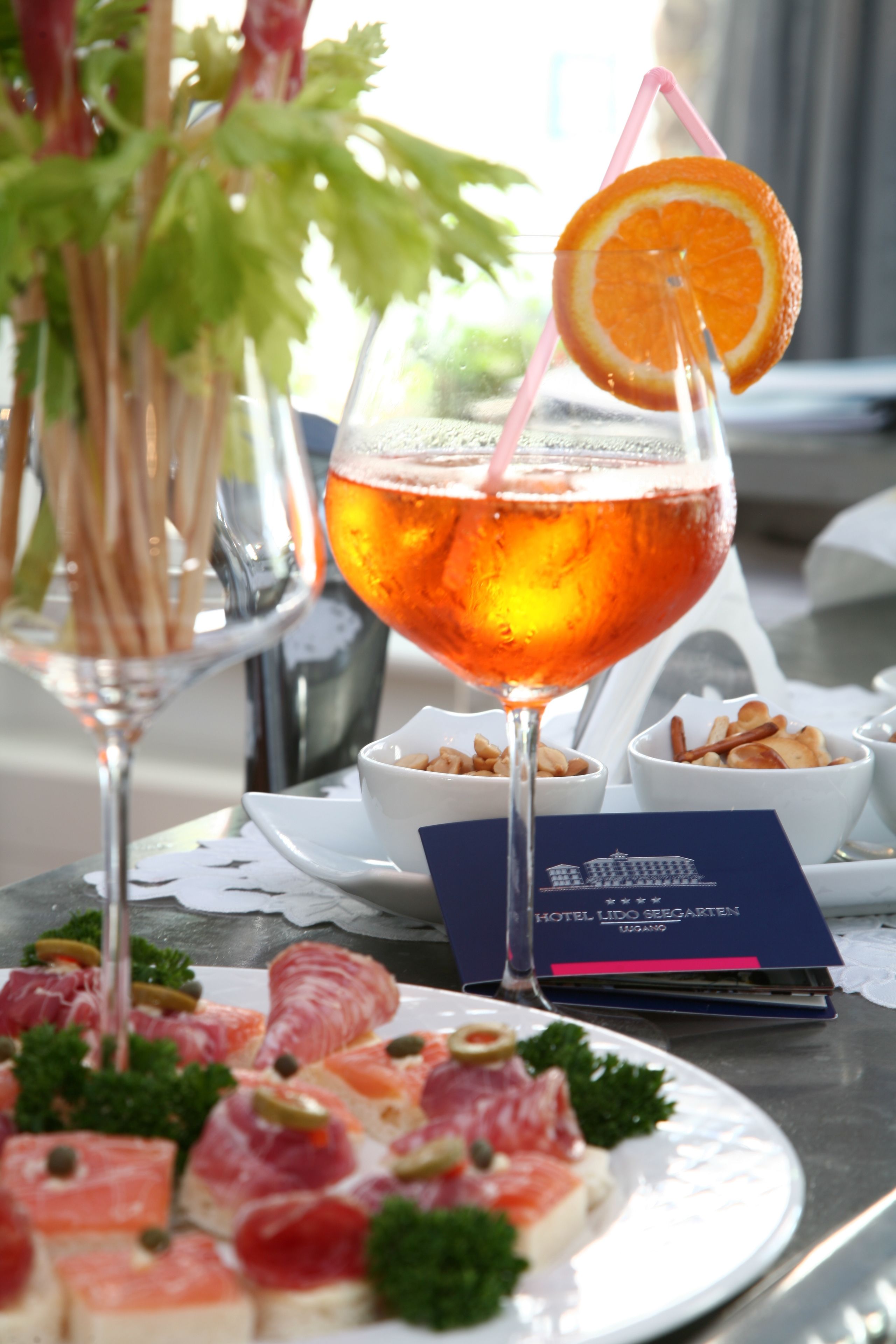 A table with a glass of red wine, a cocktail with an orange slice, and a plate of appetizers.