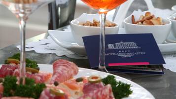 A table with a glass of red wine, a cocktail with an orange slice, and a plate of appetizers.