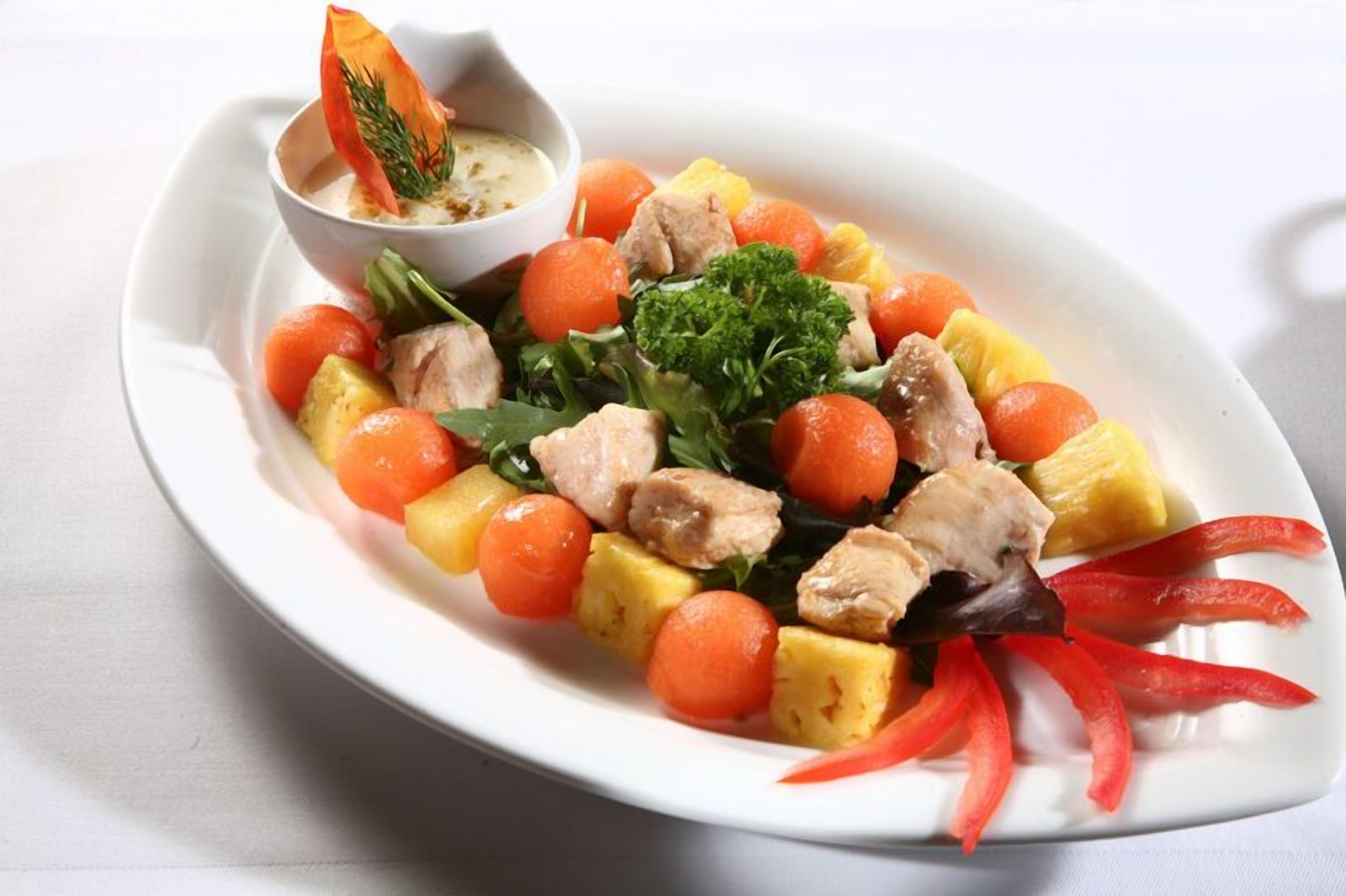 Un plato blanco con ensalada de pollo, zanahorias y piña, acompañado de un tazón pequeño de salsa.